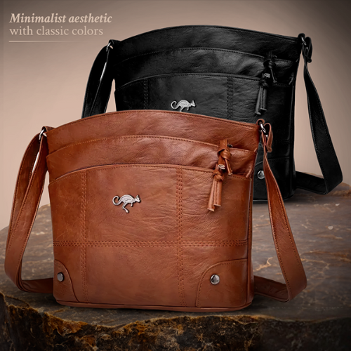 A brown leather shoulder bag with a curved silhouette, external pockets, and a secure zip closure, displayed on a natural stone surface.